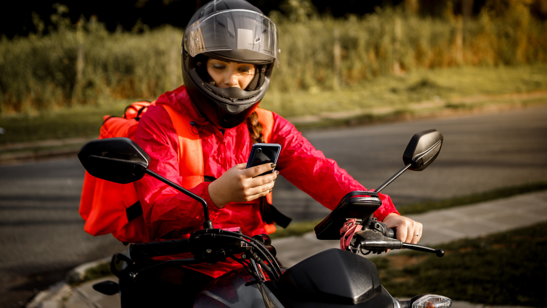 Entregadora de moto parado no semáforo conferindo a rota de entrega no celular